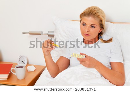 a woman in bed sick and has a fever thermometer.