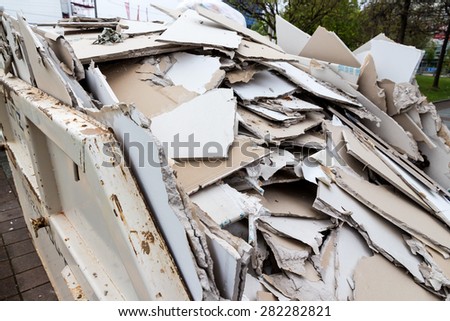 in a waste container stacks sheets of plasterboard for their disposal