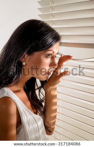 a young woman watching something through the blinds of her window
