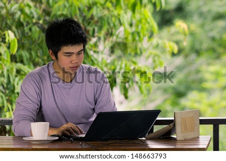 young man in purple t-shirt keying notebook  with tablet and coffee cup at terrace