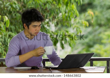 young man in purple t-shirt holding coffee cup and using notebook and tablet at terrace