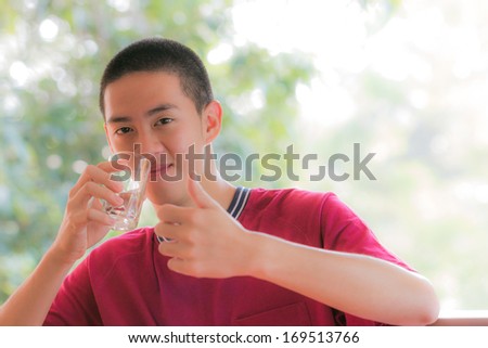 cool young man in red t-shirt holding a glass of water with thump up