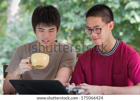 two cool young man in t-shirt smiling and playing note book with a cup of coffee