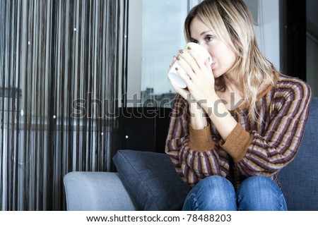 blond woman holding a beverage mug and looking through her window
