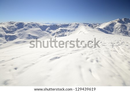 Scenic view of the alpine arc from the smooth summit ridge with powder snow and soft back country ski tracks in the foreground.