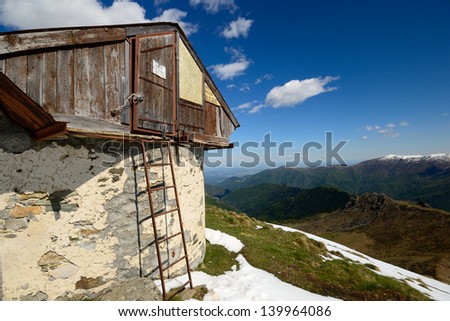 Emergency wooden alpine hut and old weather shelter in majestic high mountain scenery in spring season. Location: Gran Paradiso National Park, western Alps, Italy.