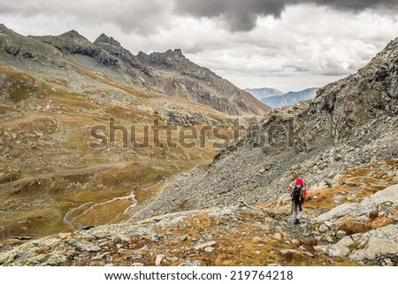 Hiker walking on dangerous footpath crossing a steep rocky slope with great panoramic view and dramatic sky.