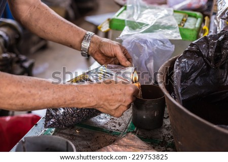 Market vendor sealing bag of freshly roasted black coffee beans for sell in indonesian market (Sulawesi). Unrecognizable person, arms and hands only shown.