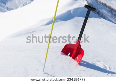 Red shovel and graduated probe for avalanche safety in powder fresh snow. Winter season in the italian Alps.