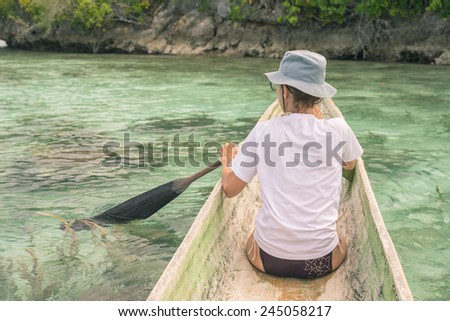 Female tourist paddling on traditional wooden canoe on blue lagoon in the remote Togean Islands, Central Sulawesi, Indonesia. Selective focus, low contrast, low saturation, toned im