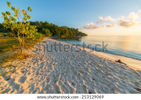 Golden sunrise on desert white sandy beach. Tourist resort in the remote Togean (or Togian) Islands, Central Sulawesi, Indonesia, upgrowing travel destination for young hipsters.