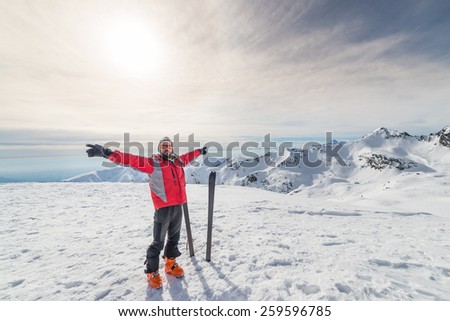 Male alpinist with arms outstretched near pair of back country ski on the mountain summit. Shot in backlight, stunning panoramic view of the alpine arc. Concept of success and conquering the top.