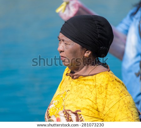 Ampana, Indonesia - August 23, 2014: Telephoto view of unidentified woman of togean ethnicity, dressed with bright yellow t-shirt and black headscarf in the port of Ampana, Central Sulawesi, Indonesia