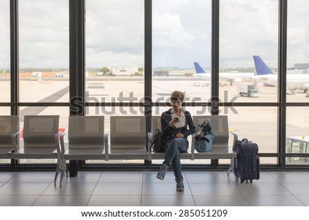Business woman sitting in airport terminal with suitcase and waiting for departure while using mobile phone. Concept of people sharing informations with new technology while traveling.