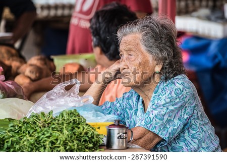 Kuching, Malaysia - August 10, 2014: Portrait of a bored senior woman managing a vegetable market stall in the popular Satok Weekend Market in Kuching, Borneo, Malaysia.
