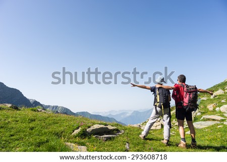 Couple of hiker with outstretched arms reaching the goal at the mountain top and looking at the wide panorama. Summer adventures and exploration on the Alps. Wide angle view from above.