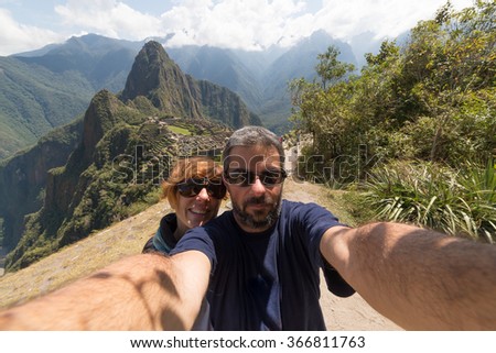 Couple taking selfie on the terraces above Machu Picchu, the most visited travel destination in Peru. Concpet of adventures in South America and people traveling aroudn the world.