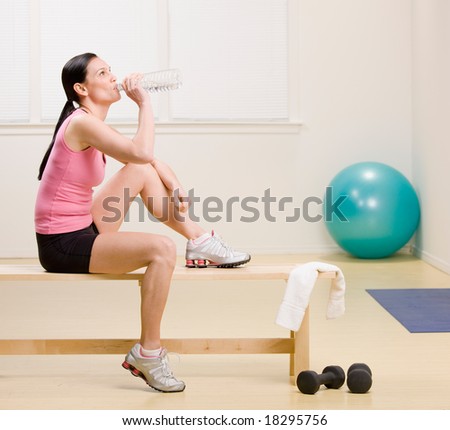 Woman drinking water and resting on bench in fitness studio
