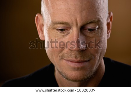 Close up studio shot of bald man with goatee and mustache looking down