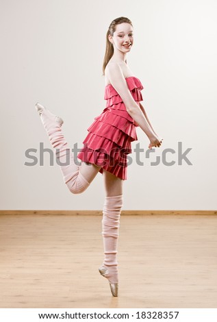 Ballerina in frilly dress and leg warmers balancing on toe in dance studio