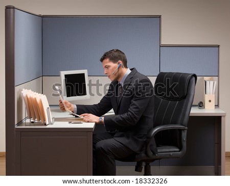 Serious young businessman with headset working at desk in cubicle