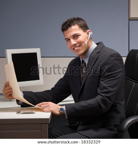 Happy young businessman with headset working at desk in cubicle