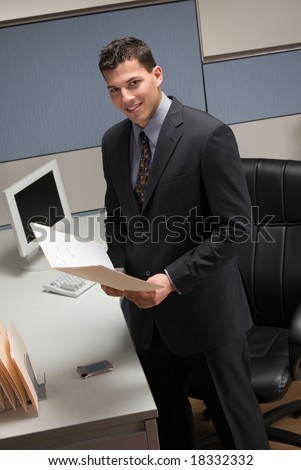 Young businessman standing at desk in cubicle holding file folder