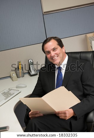 Smiling businessman holding file folder at desk in cubicle