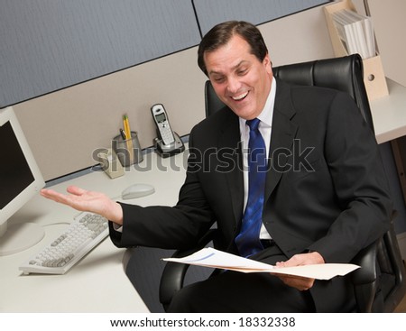 Excited businessman reviewing file folder at desk in cubicle
