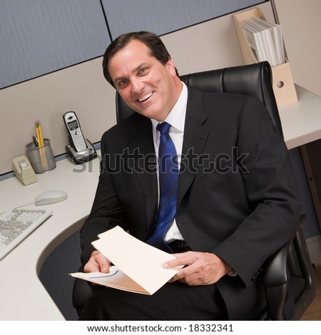 Happy businessman holding file folder at desk in cubicle