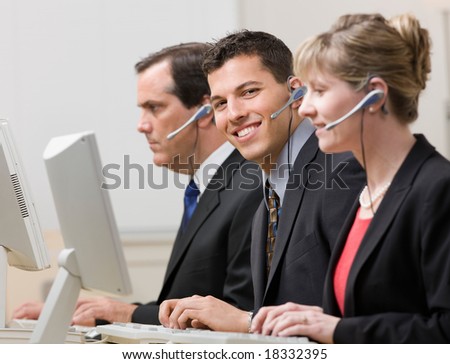 Happy co-workers in headsets working at computers in call center
