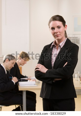 Serious businesswoman posing with co-workers meeting in conference room behind her