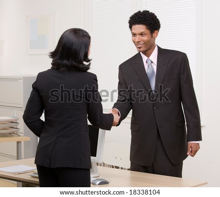 Confident woman shaking hands with co-worker at desk in agreement