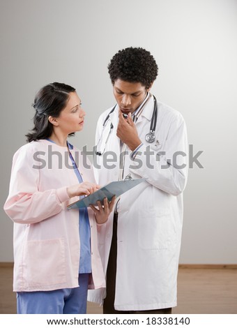 Serious doctor in lab coat listening to nurse explain medical chart