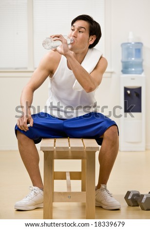 Fatigued man in sportswear drinking water from bottle in health club