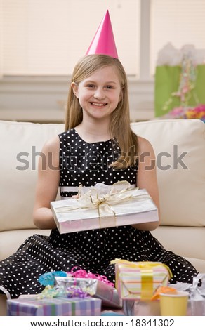 Happy, excited girl in party hat opens birthday gifts