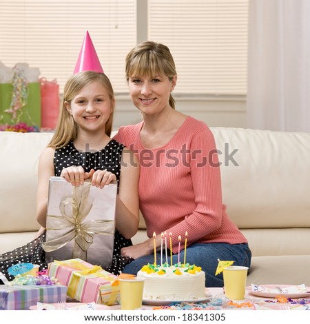 Happy, excited girl and mother sit with birthday gifts and birthday cake