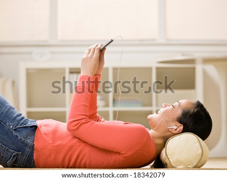 Woman listening to entertaining music on mp3 player while laying on floor