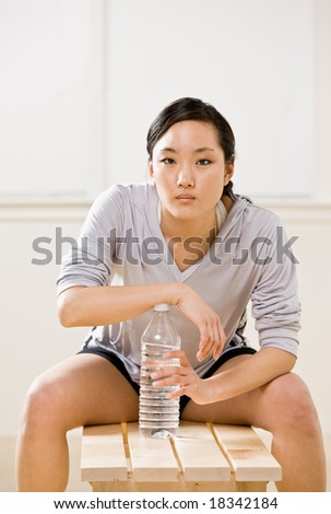 Fatigued woman drinking water from bottle in health club