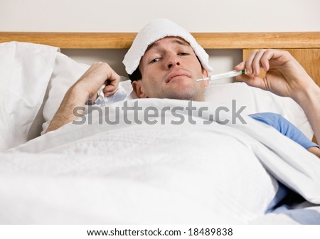 Sick man with fever laying in bed taking temperature with thermometer