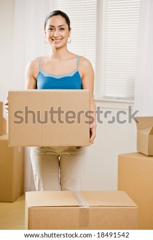 Happy woman moving into new home and carrying cardboard box