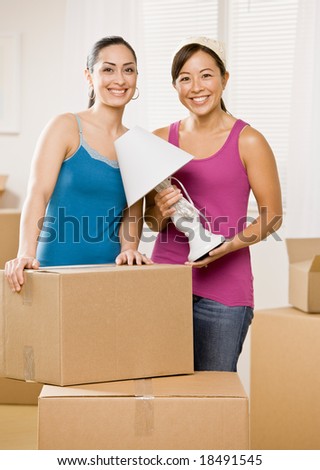 Happy women moving into new home and unpacking cardboard box
