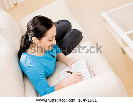 Relaxed woman laying on sofa in livingroom writing in diary