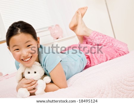 stock photo Happy barefoot girl laying on bed with stuffed animal