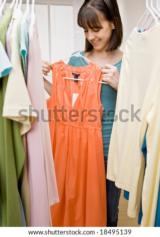 Curious teenager searching in closet for something to wear holding up dress