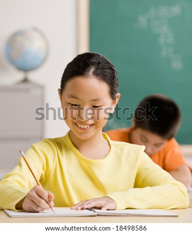 Happy student writing in notebook in school classroom