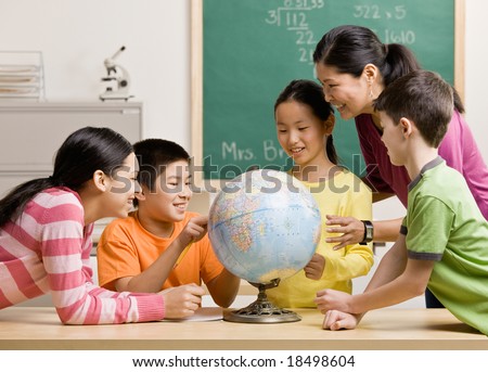 Teacher and students viewing globe in geography classroom