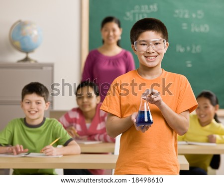 Student wearing safety goggles holds beaker of liquid in science classroom
