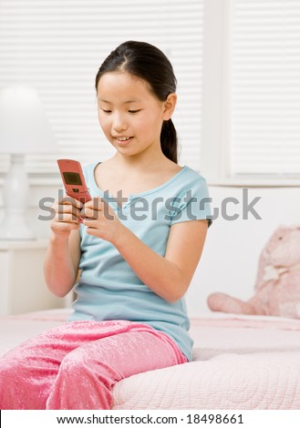 Girl in pajamas in bedroom text messaging with cell phone