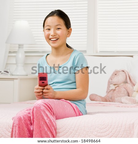 Girl in pajamas in bedroom text messaging with cell phone